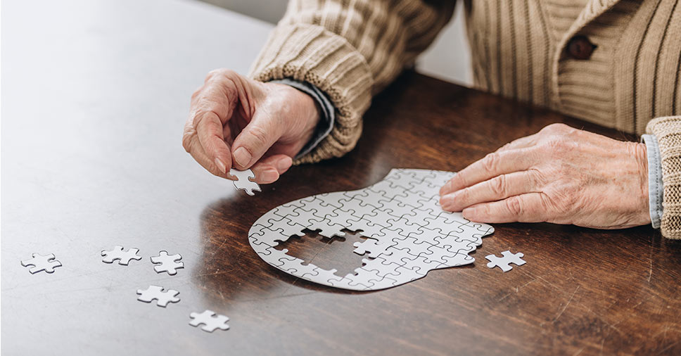 Vemos uma pessoa com demência na terceira idade montando um quebra-cabeças.
