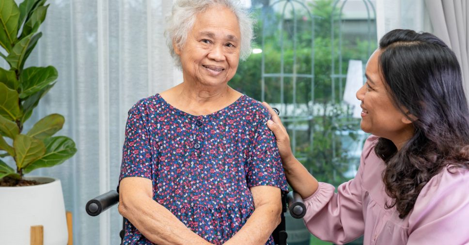 Idosa sorridente em cadeira de rodas recebe amparo e cuidados com idosos no dia a dia.